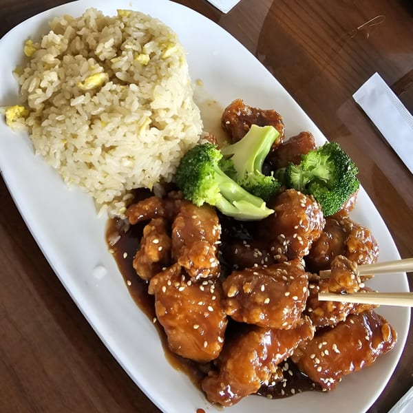 Spikey Ty's General Tso's chicken with broccoli, fried rice, and chopsticks on a white plate.