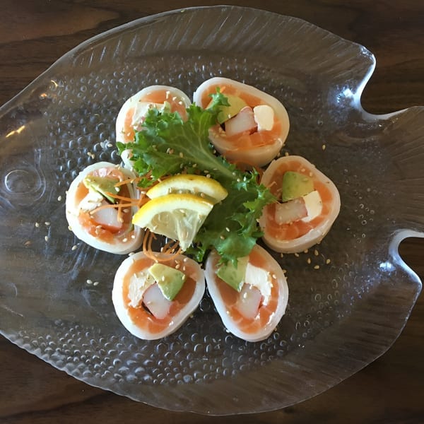 Six salmon and avocado sushi rolls with lettuce and lemon on a fish-shaped glass plate.